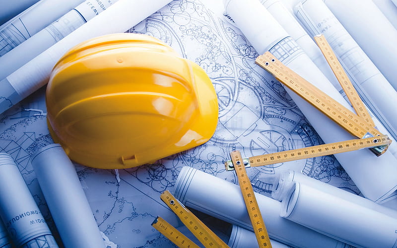 a yellow hardhat and rulers laying on design plans surrounded by rolled up plans
